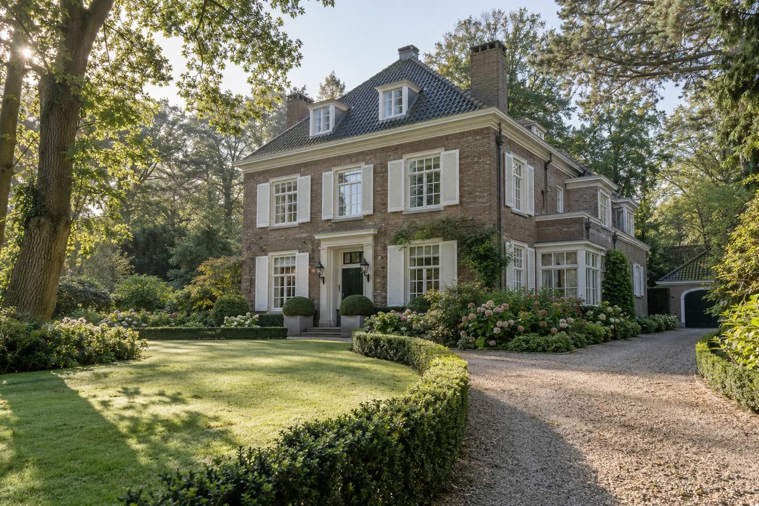 Vrijstaande villa met witte gevel en houten kozijnen op een groot perceel tussen hoge bomen en hagen in Wassenaar